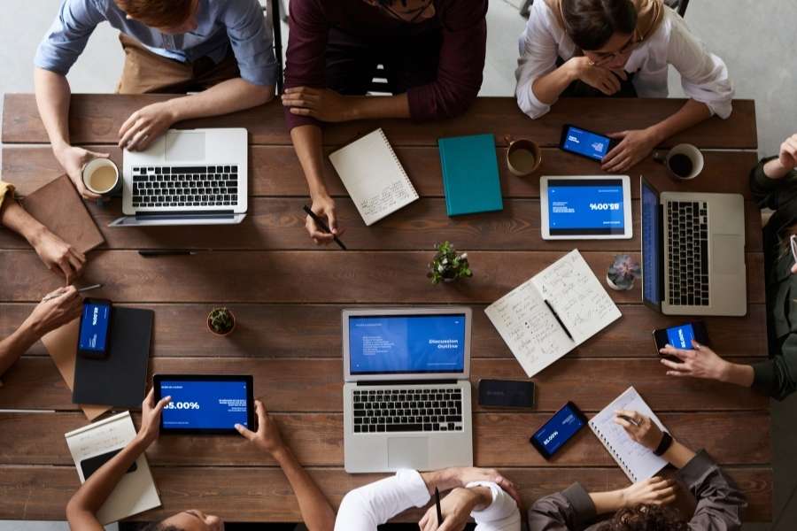 Vue de dessus d'une réunion de travail collaborative autour d'une table avec des écrans affichant une IA pour l'optimisation du maillage interne.